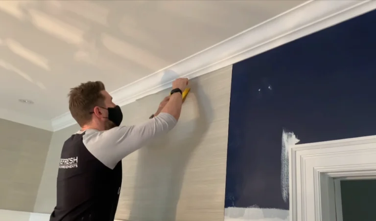 Professional wallpaper installer trimming grasscloth wallpaper at ceiling line in Denver home