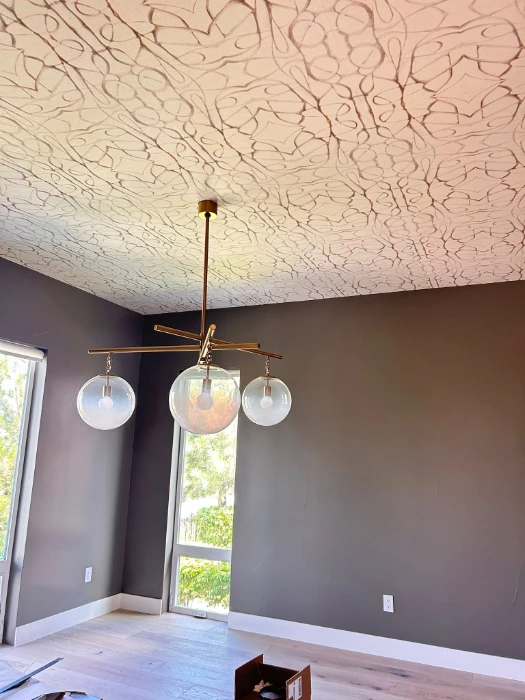 Cream textured wallpaper applied to the ceiling of a Denver room with deep plum walls and a brass pendant light