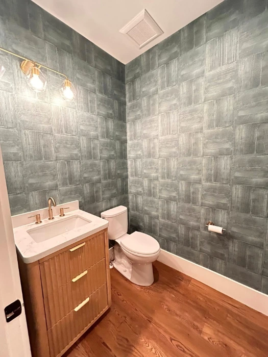 Grey-green textured block-pattern wallpaper in a Denver powder room with a wood vanity and gold fixtures